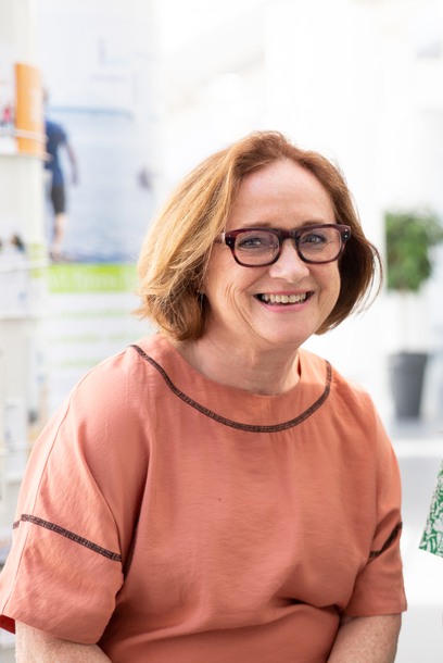 Kvinna i 60-årsåldern i rostrosa topp, leende, glasögon