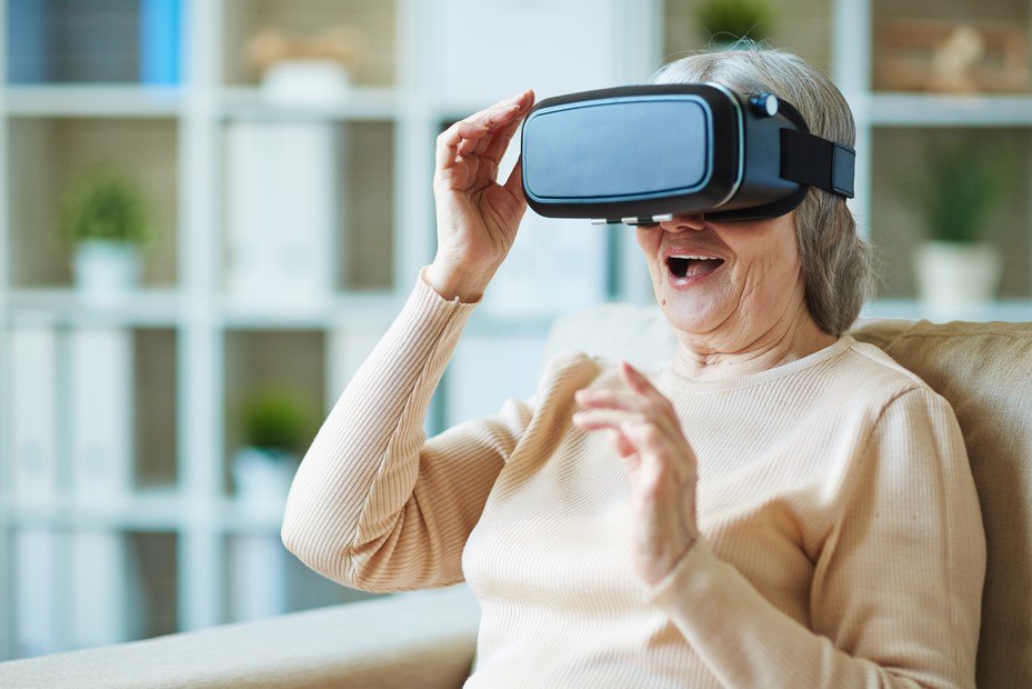 Gråhårig dam med VR-glasögon sitter i en fåtölj och ser förtjust ut.