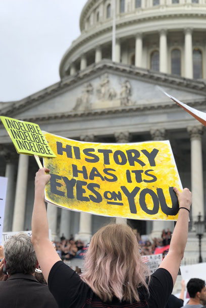 Demonstrant med gul skylt, kongressen i Washington i bakgrunden