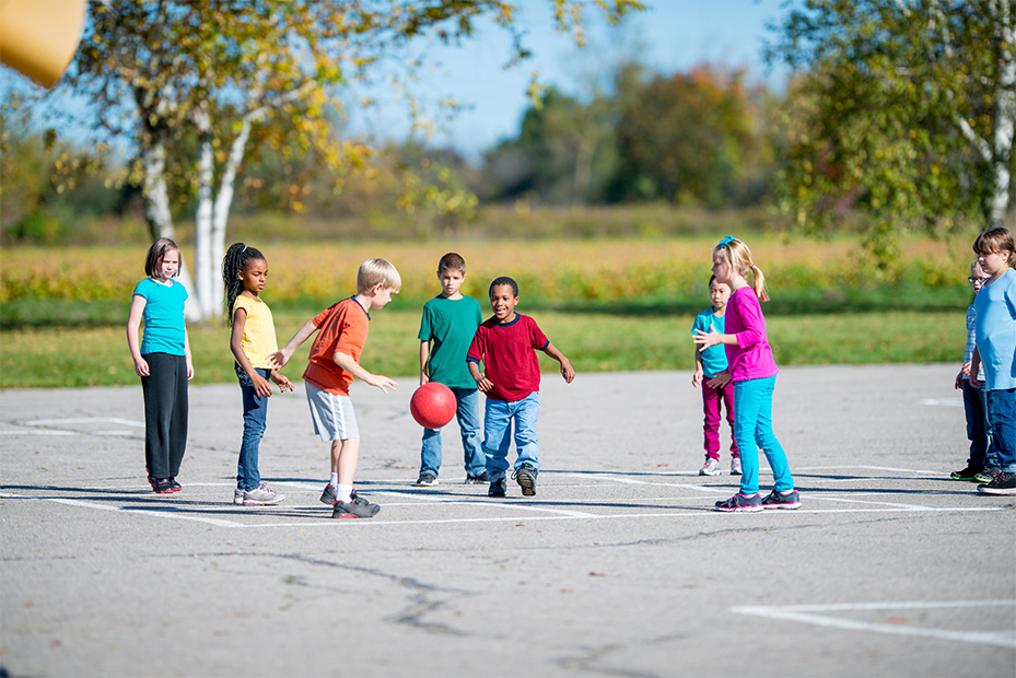 Barn leker med en boll på en asfalterad plan med vita rutor