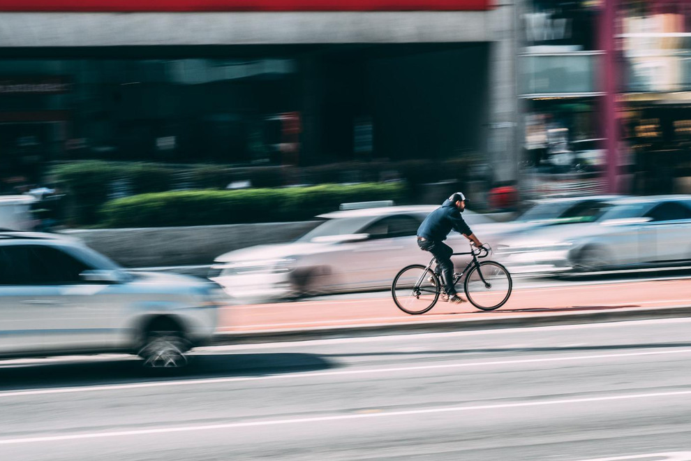 En cyklist cyklar på en bred väg mellan bilar. 