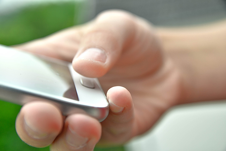 En hand håller i en mobiltelefon och tummen hålls över en knapp på mobilen.