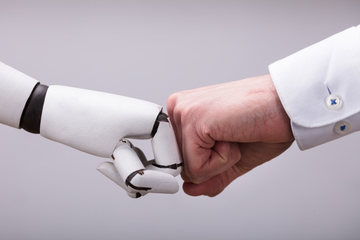 En mänsklig hand och en robothand möter varandra med knutna händer.